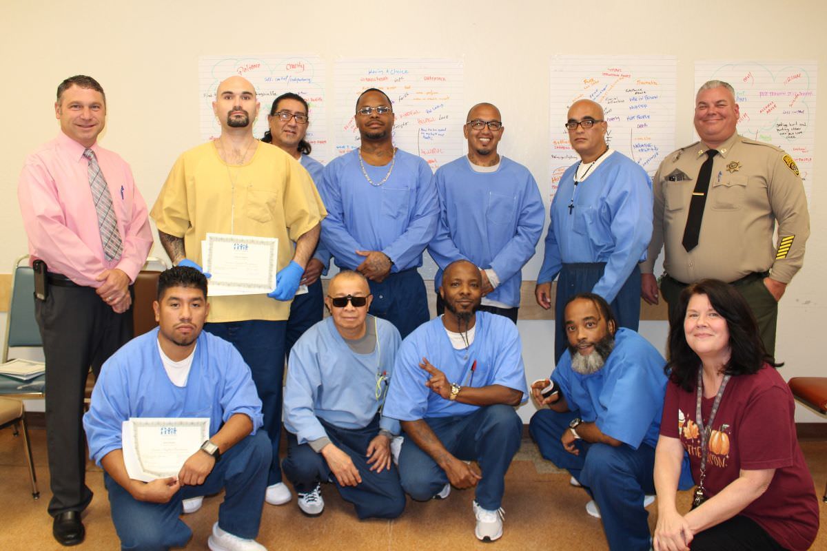 A class of incarcerated men with Friends Outside staff and a corrections officer, holding certificates.