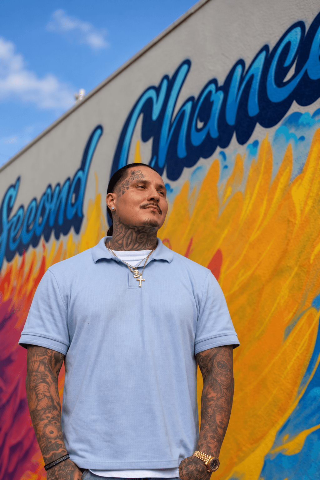 A man in a light blue shirt stands in front of the Rising Phoenix mural.