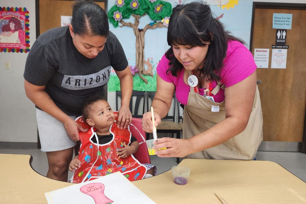A Visitor Center staff member helps a toddler paint while his mother watches.